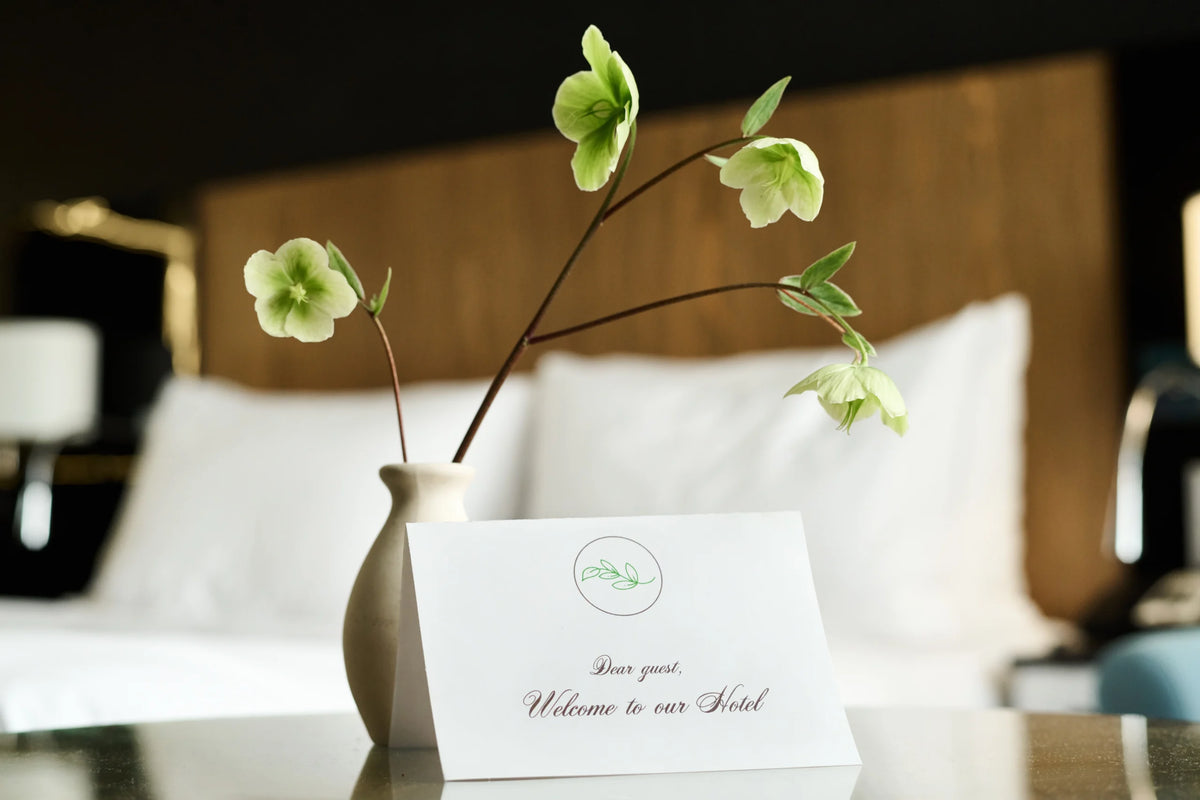A welcome card and flowers on a hotel bedside table